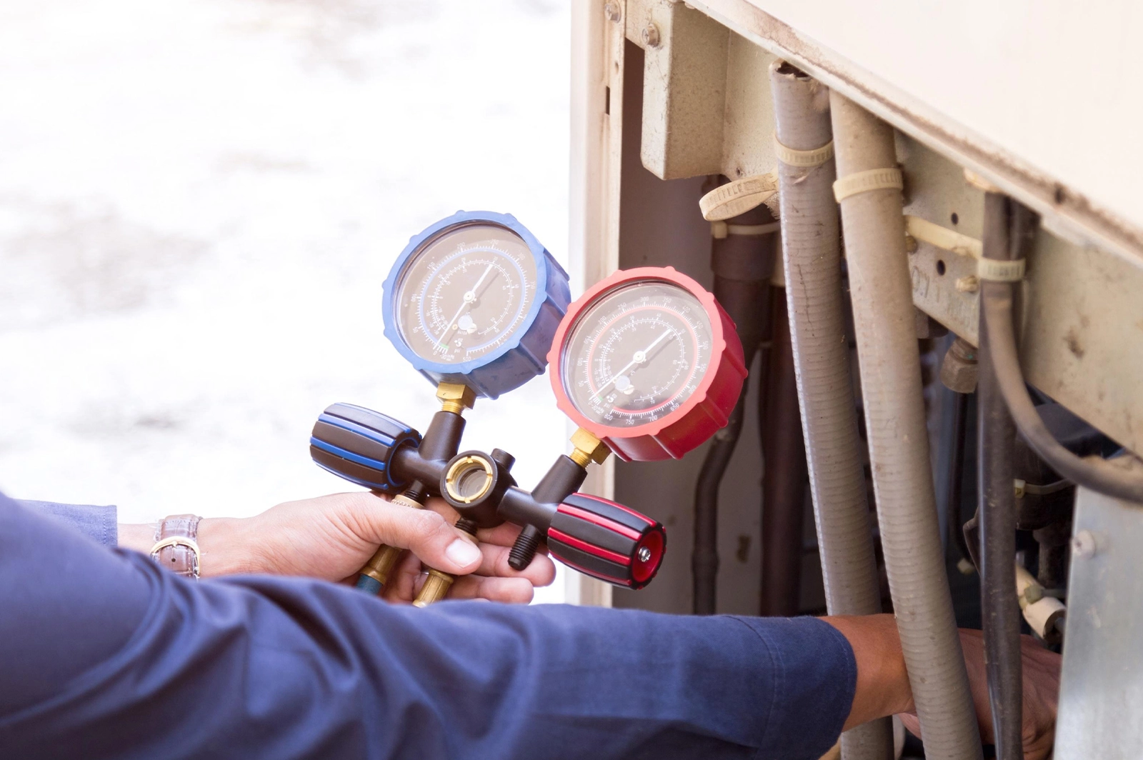 Technician using a manifold gauge set to check pressure in an air conditioning unit.