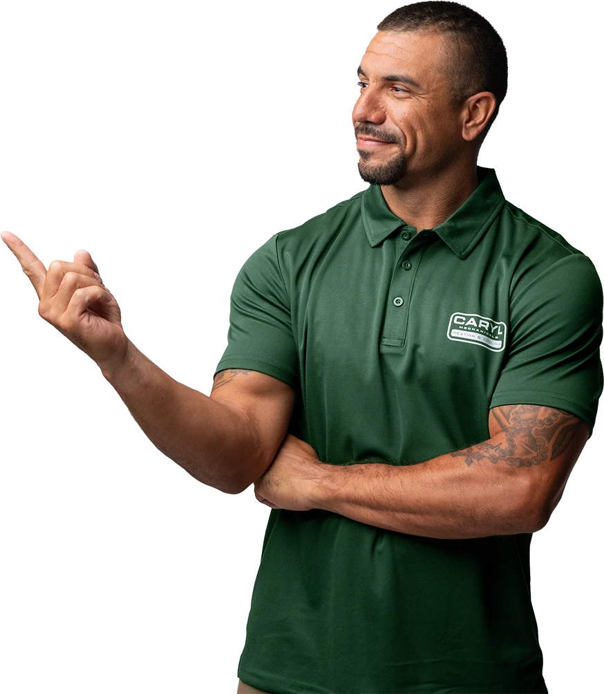 Man in a green polo shirt with a “Cary” logo stands with folded arms, pointing to the left and smiling, against a plain white background.